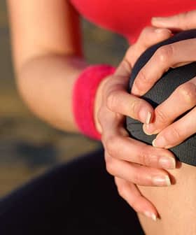 Individual with a red shirt holding their knee with both hands, indicating discomfort or pain. - Olive Oil Times