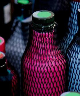 Various bottles covered in mesh with colored caps and labels arranged closely together. - Olive Oil Times