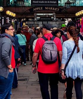People walking through Apple Market with various stalls and merchandise on display. - Olive Oil Times