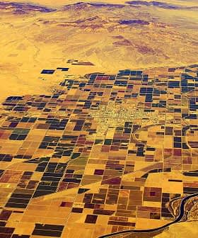 Aerial view of a patchwork of agricultural fields in a desert landscape with a river running through. - Olive Oil Times