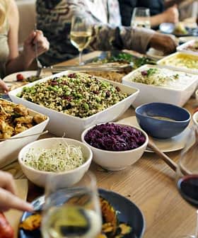 A dining table filled with various dishes, including salads, meats, and side dishes, with people dining around it. - Olive Oil Times