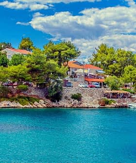 A coastal scene featuring houses on a hillside and boats in clear blue water. - Olive Oil Times