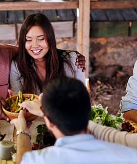 A diverse group of people sitting around a table sharing food in an outdoor setting. - Olive Oil Times