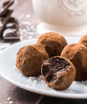 A plate of chocolate truffles coated in cocoa powder with one truffle partially bitten into. - Olive Oil Times