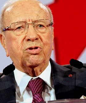 Elderly man in a suit speaking passionately at a podium with raised hands. - Olive Oil Times