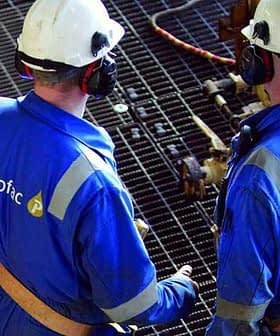 Two Petrofac workers wearing blue uniforms and safety helmets discussing on a metal grid surface. - Olive Oil Times
