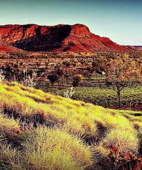 A red rock formation surrounded by grassland and sparse trees under a clear sky. - Olive Oil Times