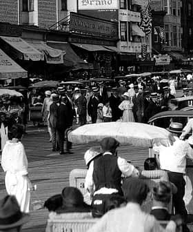Black and white photograph of a busy boardwalk filled with pedestrians and horse-drawn carriages. - Olive Oil Times