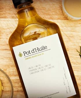 Bottle of olive oil labeled 'Pot d'Huile' with garlic, mustard, and herbs on a wooden surface. - Olive Oil Times