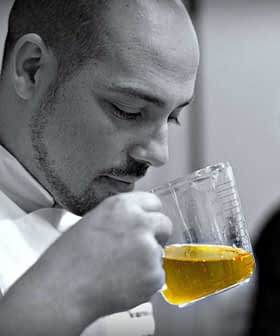 Chef smelling olive oil from a measuring cup while another person is in the background. - Olive Oil Times