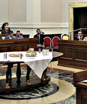 A legislative assembly room with attendees seated at tables during a meeting. - Olive Oil Times