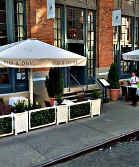 Outdoor dining area with white umbrellas and tables at Fig & Olive restaurant. - Olive Oil Times