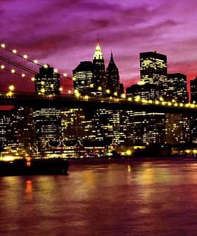 Brooklyn Bridge illuminated at night with the New York City skyline in the background under a purple sky. - Olive Oil Times