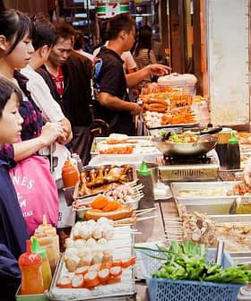 A street food vendor serving various dishes to a group of customers in a market setting. - Olive Oil Times