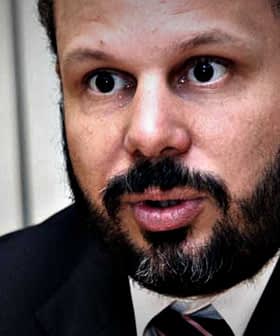 Man with a beard wearing a suit and tie, speaking during a meeting or interview. - Olive Oil Times