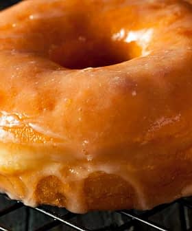 A close-up of a glazed doughnut resting on a wire cooling rack. - Olive Oil Times