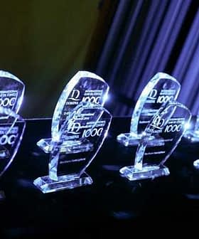 Row of crystal awards with engraved text on a dark surface illuminated by blue light. - Olive Oil Times