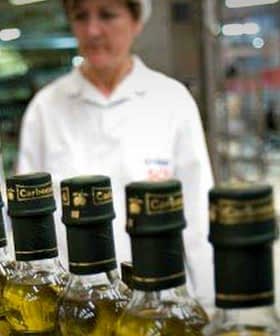 Row of olive oil bottles on a production line with a worker in the background. - Olive Oil Times