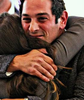 A man and a woman embracing each other in a social gathering, both smiling. - Olive Oil Times