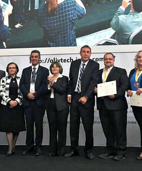 A group of individuals standing together on stage holding certificates at an event. - Olive Oil Times