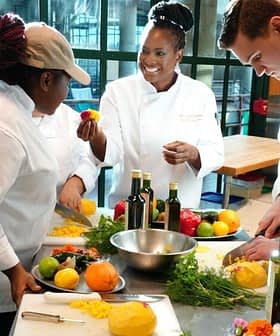 Three chefs in a culinary class preparing ingredients with fruits and vegetables on a table. - Olive Oil Times