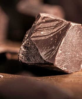 Pieces of dark chocolate scattered on a wooden surface with a textured appearance. - Olive Oil Times