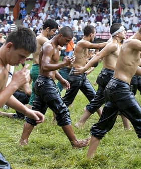 Young men in wet clothing walking in a line during a traditional event on a grassy field. - Olive Oil Times