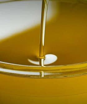 A clear bowl filled with olive oil, with olives placed beside it on a wooden surface. - Olive Oil Times