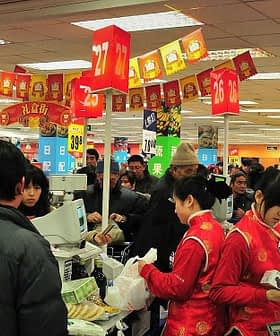 Crowd of shoppers and cashiers at a busy supermarket checkout area with red decorations. - Olive Oil Times