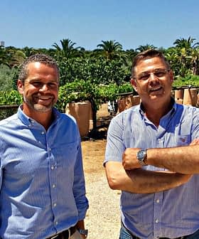 Two men standing in an olive grove, smiling and posing for the camera. - Olive Oil Times