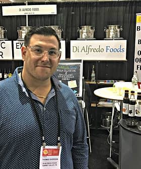 Man standing in front of a booth displaying balsamic vinegar and olive oil products at a trade show. - Olive Oil Times