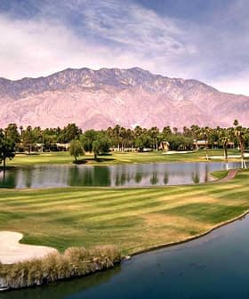 A panoramic view of a golf course featuring water hazards and palm trees with mountains in the background. - Olive Oil Times