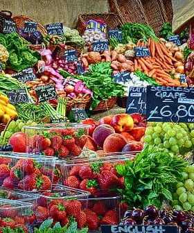A vibrant assortment of fresh fruits and vegetables arranged at a market stall with price tags. - Olive Oil Times