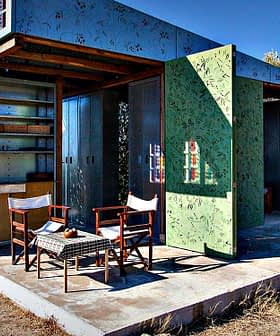 A modern outdoor structure with green walls and two wooden chairs in front of it. - Olive Oil Times