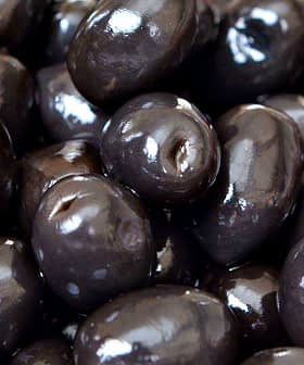 Close-up image of shiny black olives arranged closely together. - Olive Oil Times