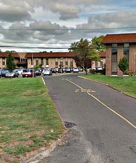 Two commercial buildings with a parking lot in front, surrounded by grass and trees. - Olive Oil Times