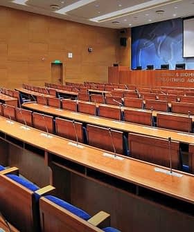 Interior view of a conference room featuring wooden seating and a presentation screen. - Olive Oil Times
