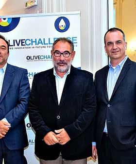 A group of seven individuals posing for a photo at an olive oil event with a banner in the background. - Olive Oil Times