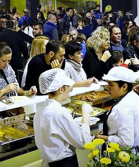 Crowd of people enjoying food at a culinary event with chefs serving dishes. - Olive Oil Times