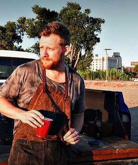Man with a beard holding a red cup while standing next to a pickup truck in an outdoor setting. - Olive Oil Times
