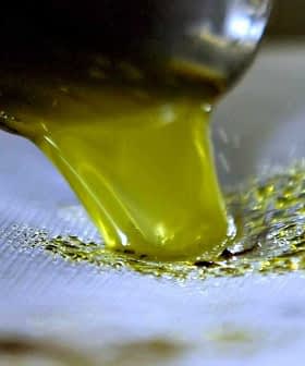 Stream of green olive oil pouring from a metal spout onto a surface. - Olive Oil Times