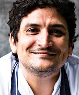 Smiling chef with curly hair wearing a white chef jacket and a gray apron. - Olive Oil Times