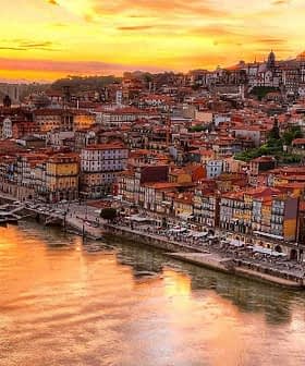 A panoramic view of Porto's riverfront at sunset with colorful buildings along the water's edge. - Olive Oil Times