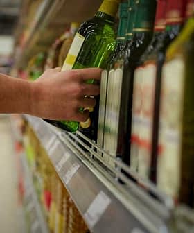 A person reaching for a bottle of olive oil on a supermarket shelf. - Olive Oil Times