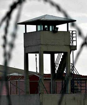 A prison watchtower surrounded by barbed wire fencing in a cloudy environment. - Olive Oil Times
