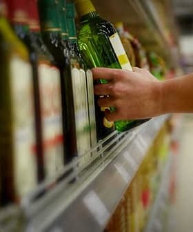 A person reaching for a green bottle of olive oil on a supermarket shelf. - Olive Oil Times