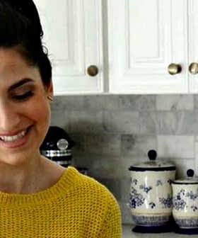 Woman with long dark hair wearing a yellow sweater while preparing food in a kitchen. - Olive Oil Times