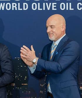 Two men at the World Olive Oil Competition award ceremony, one holding a trophy and the other applauding. - Olive Oil Times