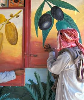 Two men in traditional attire examining wall murals depicting olives and dates. - Olive Oil Times