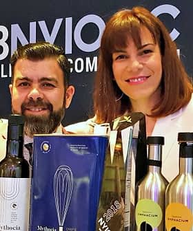 Two individuals giving thumbs up while posing with various olive oil bottles and awards. - Olive Oil Times